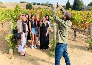 A birthday group of women posing among grapevines while their guide takes their photo