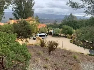 A hillside view over a Napa Valley estate with a white van in the driveway and mountains beyond