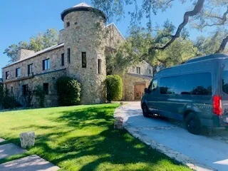 A dark Cuvée Mercedes Sprinter van parked beside a stone winery building